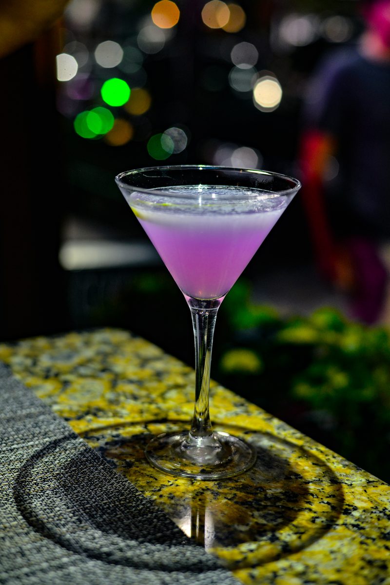 A purple martini on a granite bar top at Tresca in Boston's North End, with colored lights glowing behind it, 2018