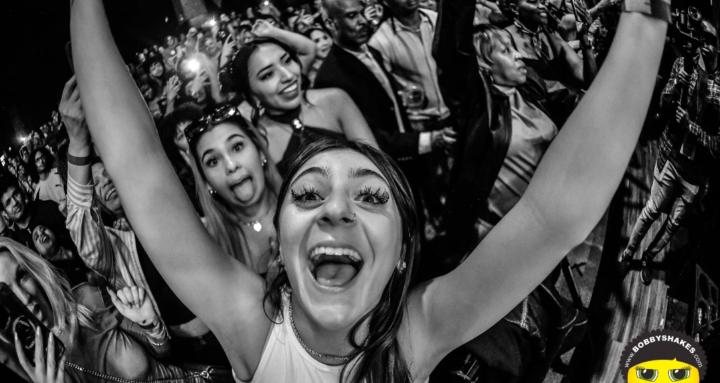 Black-and-white crowd photo by Bobby Shakes: fans with arms up at a concert